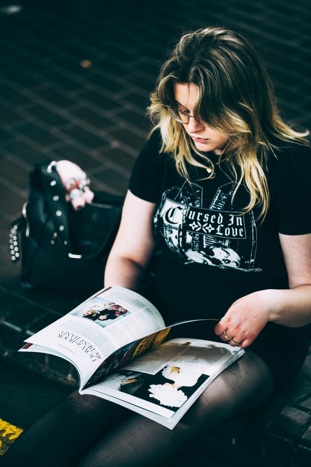 Woman in a black graphic T-shirt reading a magazine.